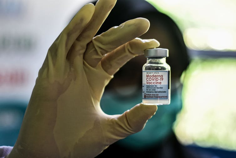 A health care worker holds up a Moderna COVID-19 vaccine vial.