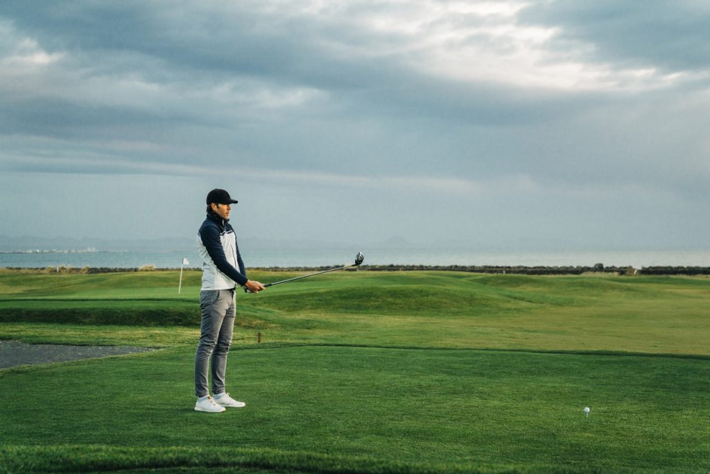 Stylish golfer on golf course wearing blue and white waterproof gold jacket.