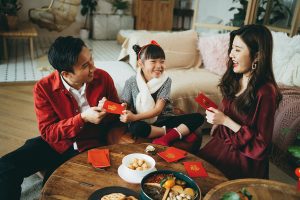 Joyful young Asian family celebrates Chinese New Year, parents giving red envelops (lai see) to their daughter and she receives them with both hands