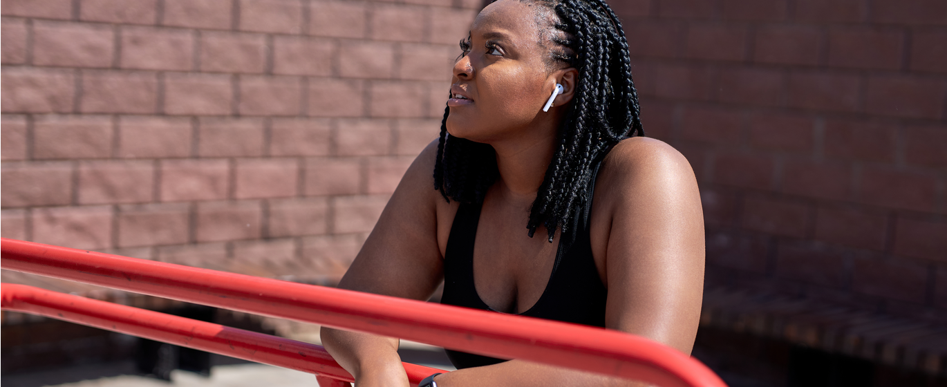 African American woman wearing headphones and workout gear looks up toward the sky, looking contemplative and optimistic