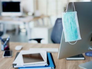 Face mask hanging on computer screen in empty office