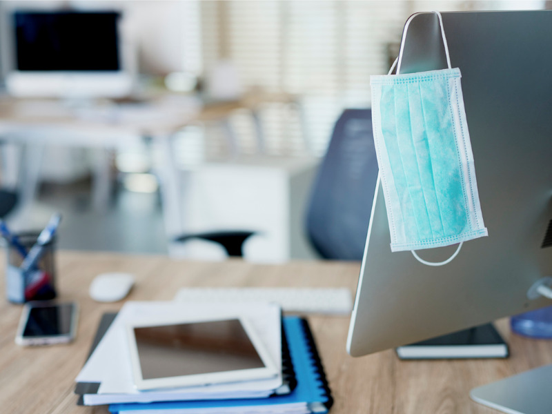 Face mask hanging on computer screen in empty office