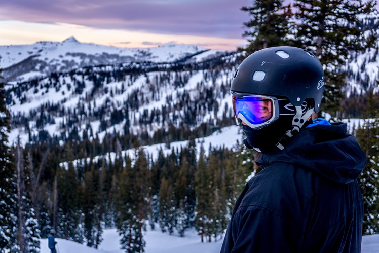 Skier with goggles and helmet standing on a snowy mountain and surrounded by trees