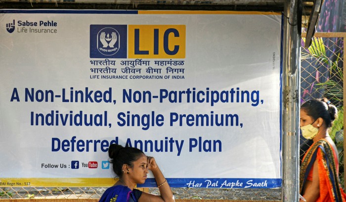 Two women next to an LIC annuity advert at a bus stop in Mumbai, India