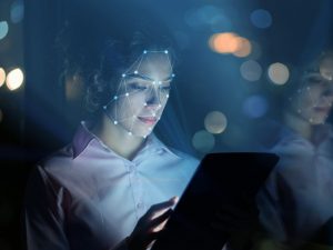 A woman's face is lit up by the blue light of the screen she is holding in her hand. It is scanning her face.