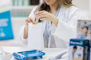 A pharmacist places a customer's prescription medication into a paper bag