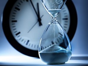 Deadline and running out of time. A sand timer hourglass in the foreground with a clock face approaching mid-night in the background. A concept illustration of shortage of time.