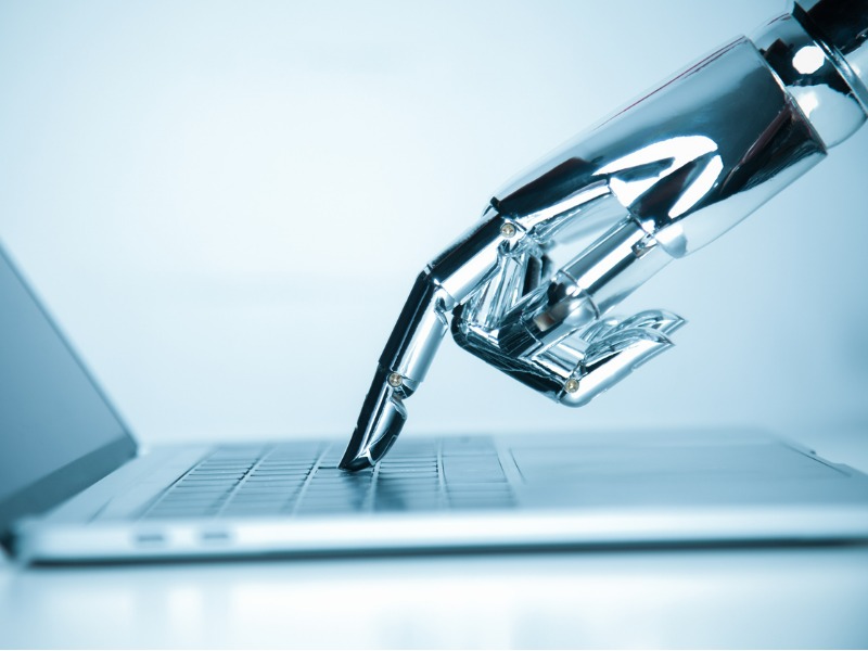 A metal robot hand is reaching out and pressing a key on a laptop.