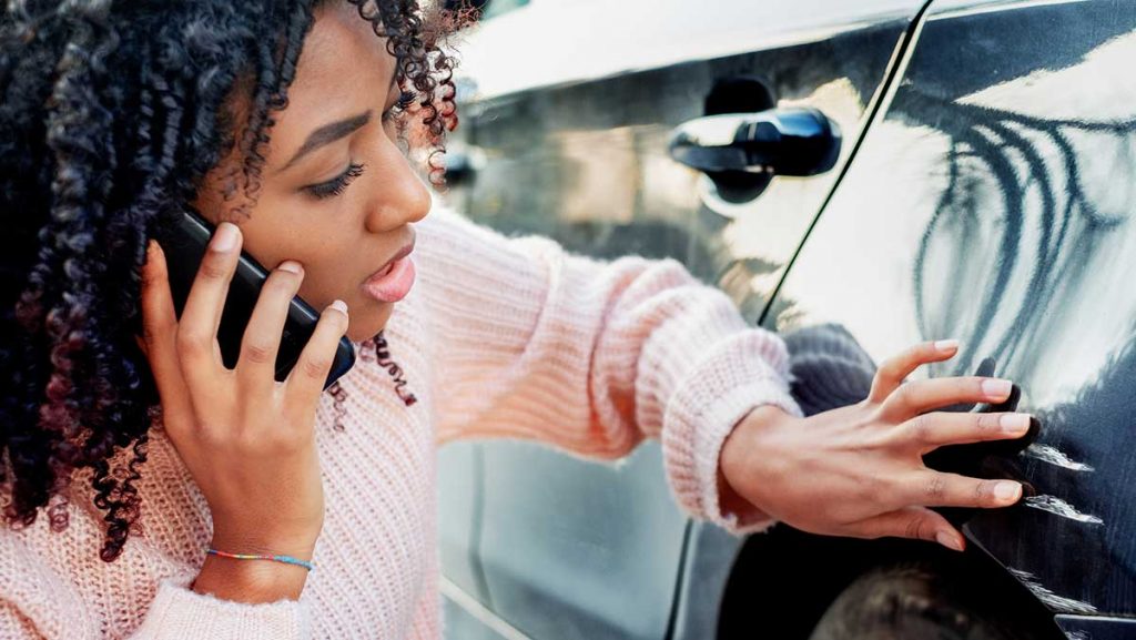 What to do when you get into a car accident - woman inspects damage to car