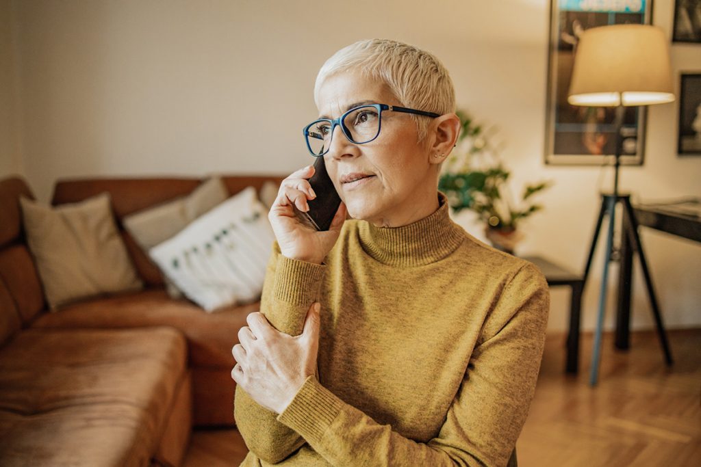 A worried senior woman with short gray hair is talking on the phone