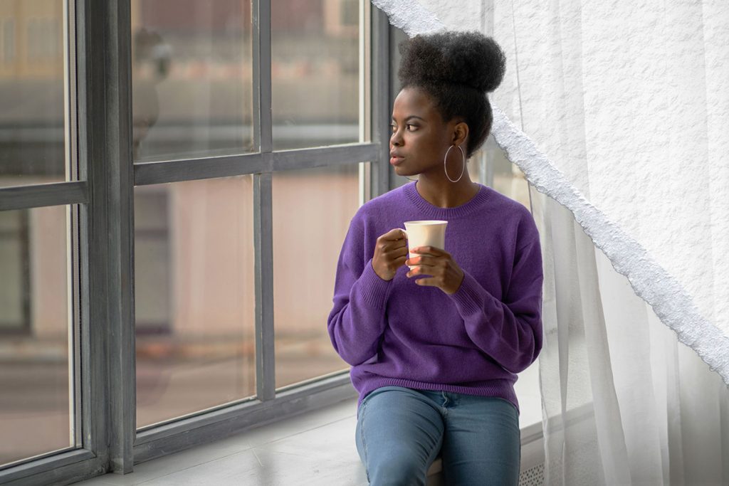 A young woman holding a cup of coffee looks out the window