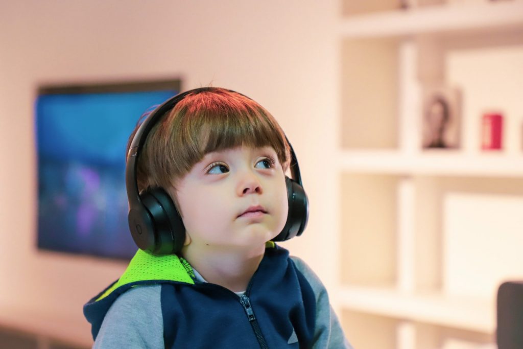 A young boy wearing a blue jacket sits with headphones over his ears.