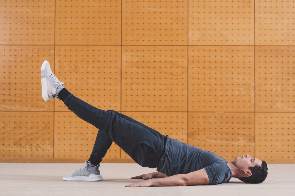 a male fitness trainer performing a single leg glute bridge