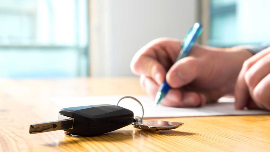 Man signing documents with car key on table - how to trade in your car