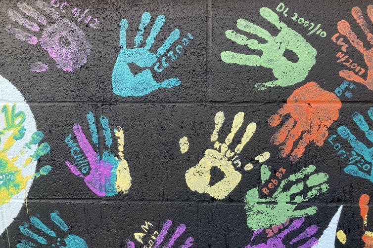 A black wall with colourful handprints and names on it