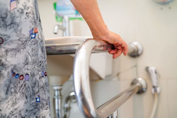 Elderly person using accessible rail to lean on while using the sink