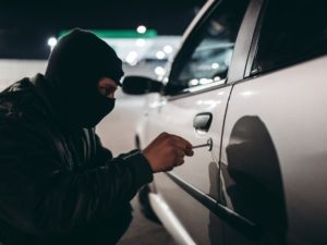 Man with a ski mask inserts a tool into a locked car door at night