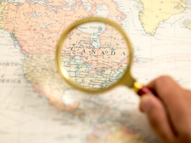 A magnifiyng glass held above a map of Canada