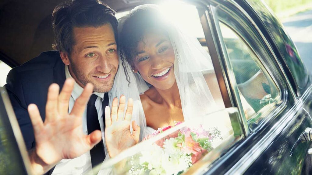 Car Insurance For Married Couples - Couple in car waving on goodbye on wedding day