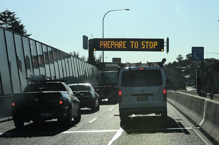 cars and a van pause in from of sign saying 'prepare to stop'