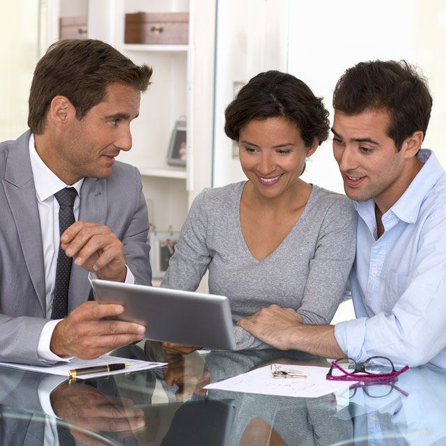 A male financial advisor, left, speaking with a young couple clients — in person.