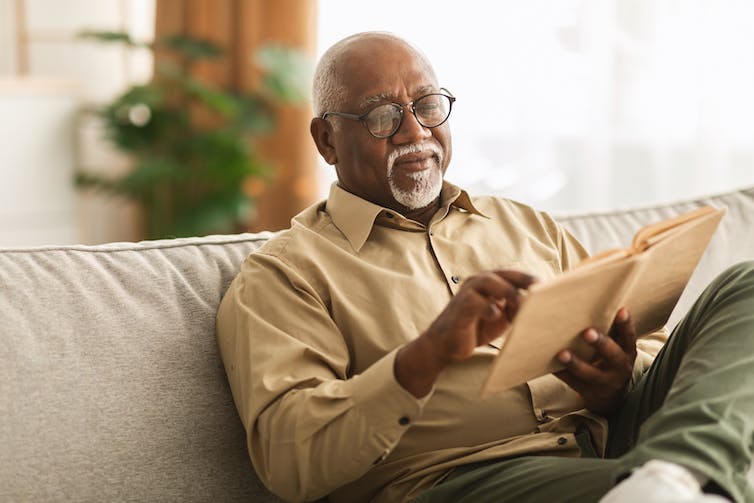 Older man with a beard reading a book sitting on a sofa