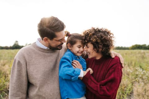 Portrait of beautiful happy family of three hugging outdoors