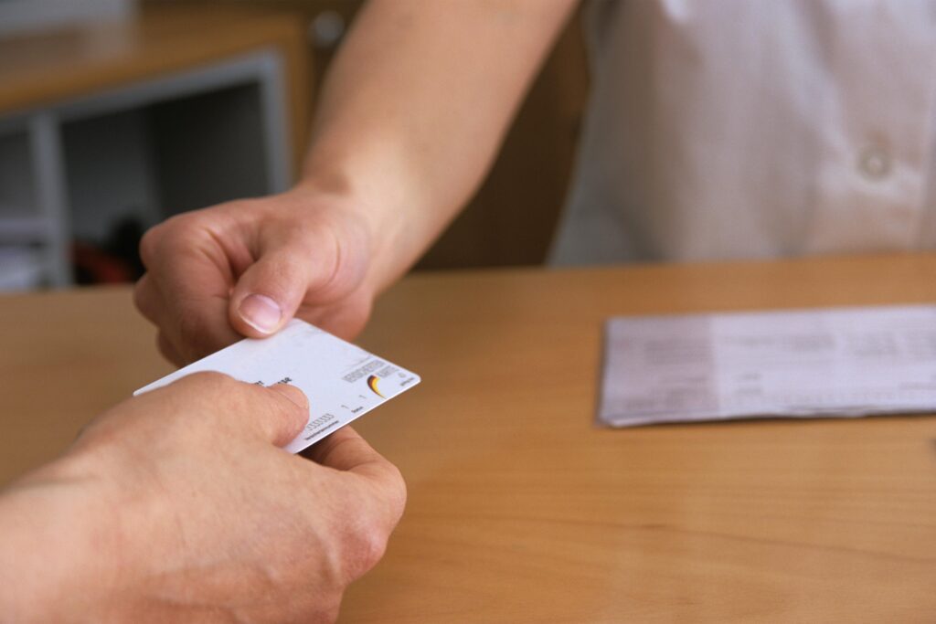 A photo shows a man handing a woman his health insurance card.