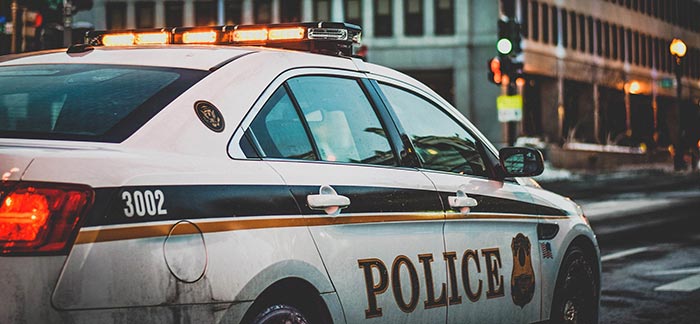 Image of police car at stoplight on an urban city street for Quotacy blog How Your Driving Record Affects Your Life Insurance