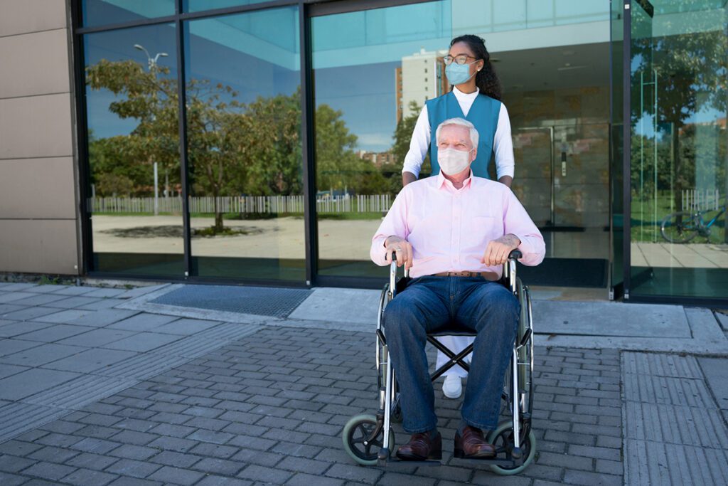Nurse pushing a senior man on a wheelchair leaving the hospital