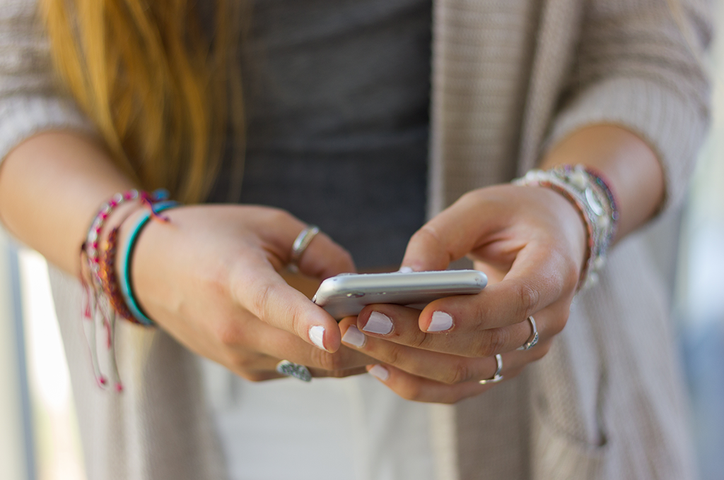 a young female student with long red hair texting on her silver mobile phone