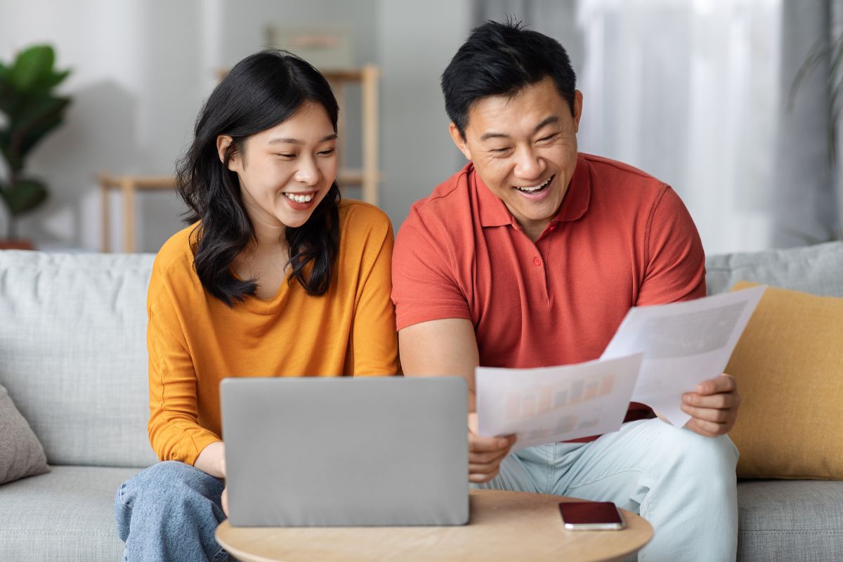 happy asian spouses paying bills online using laptop