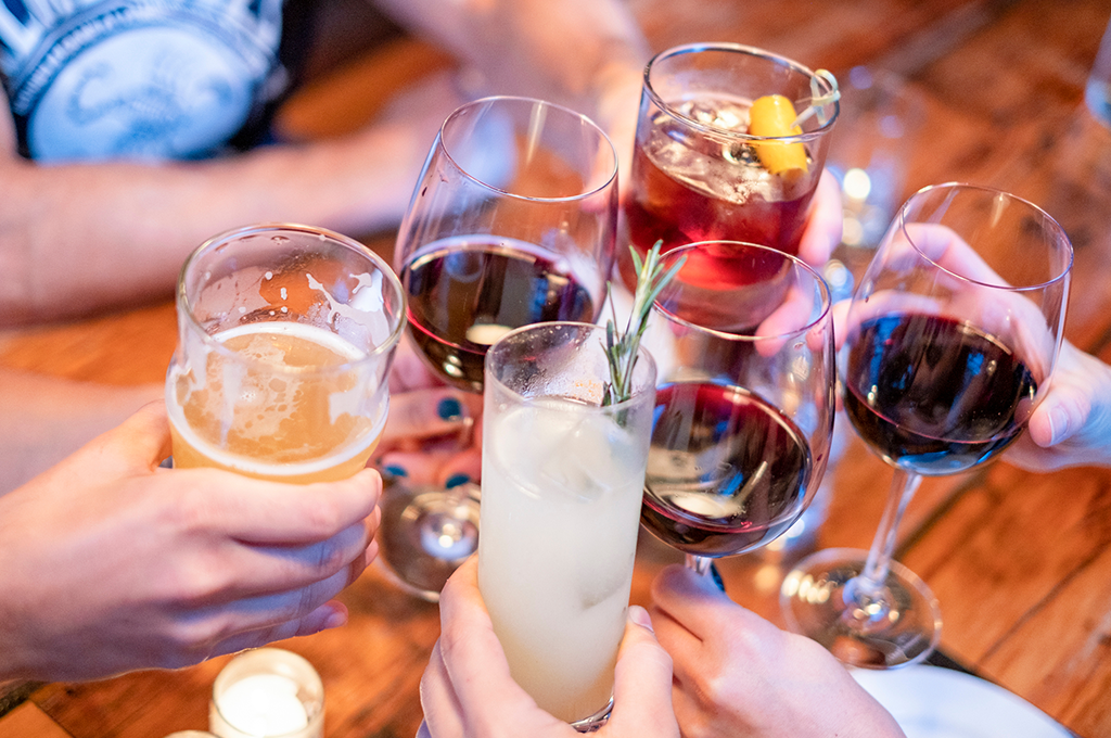 six glasses with different drinks in being toasted in a pub