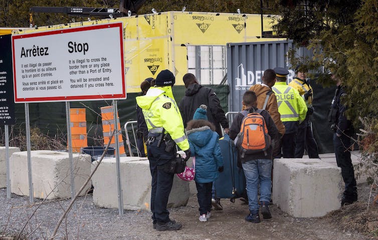 A family carrying suitcases alongside police officers in high visibility jackets.