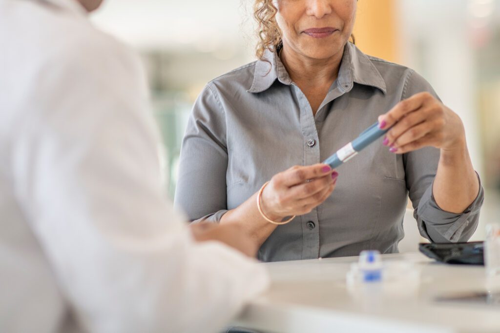 An older woman holds an insulin pen across a counter from a doctor.