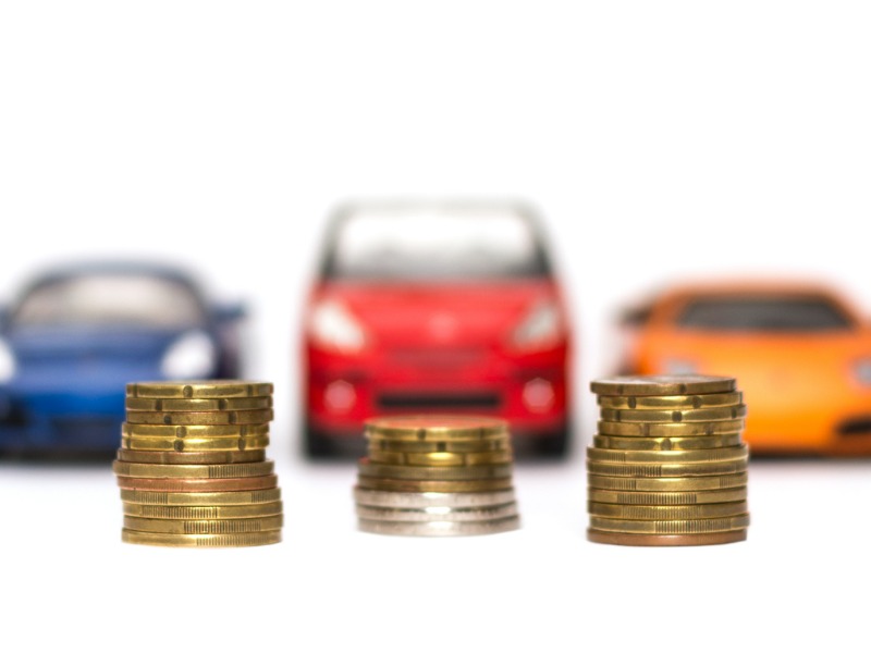 Toy auto cars in front of differing stacks of coins