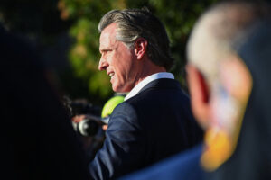 A photo shows Gavin Newsom outside speaking on a sunny day.