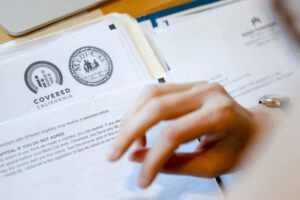 A photo shows a close-up of a person looking through Covered California paperwork.