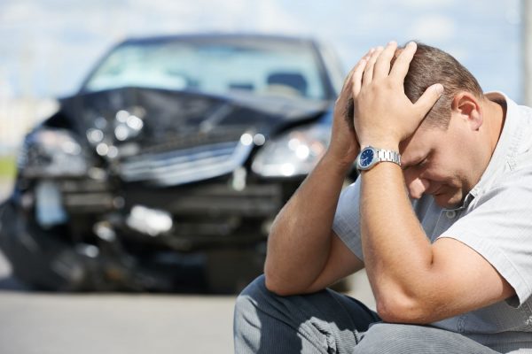 Upset man with crashed car in background