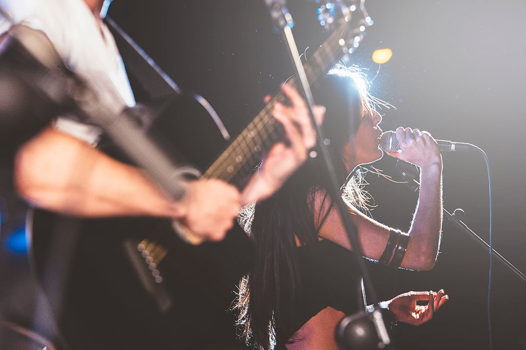 a guitarist on stage in the foreground with the female singer in focus in the background