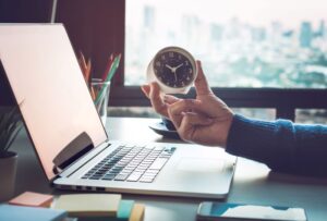 Man holding a clock over a computer laptop