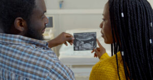 Back view of young married african couple looking at ultrasound picture at clinic.