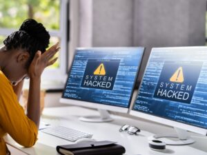 Woman lamenting as two computer screens show her system has been hacked.