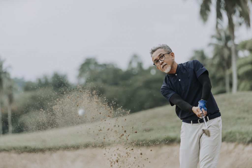 Man swinging golf club wearing golf shirt