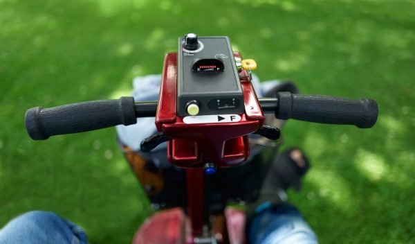 View sitting behind the handlebars of a mobility scooter on green grass in the countryside with a blurred view of their broken foot.