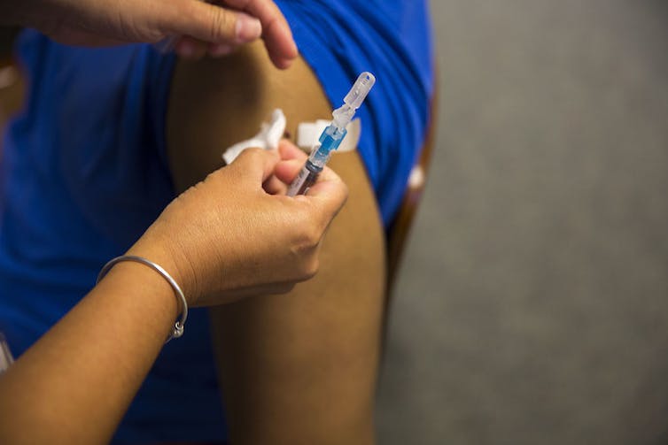 Person in a blue T-shirt being given an injection in the upper arm