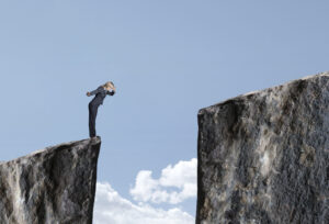 An insurance profession stands on the edge of a cliff, with a gap between another cliff.