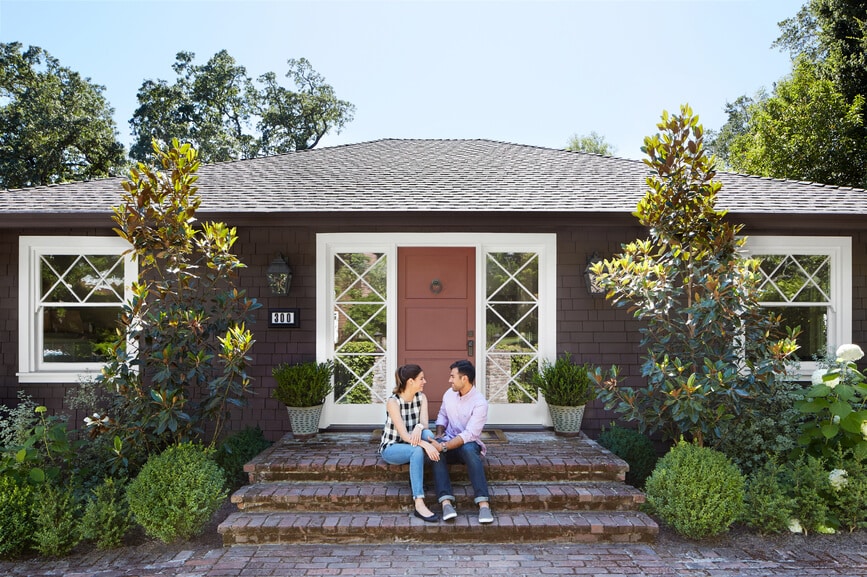 Happy couple sitting on the front steps of the new home they purchased together as their first home.