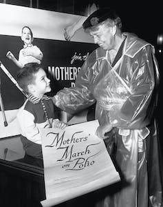 Eleanor Roosevelt smiles with a young boy holding a 'Mothers March on Polio' scroll