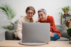 Content middle aged female with young daughter resting on sofa in living room and watching laptop at home